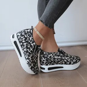 Detail von floralen Slip-on-Plateauschuhen mit dicken weißen Keilsohlen auf Holzboden