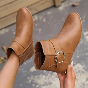 Detailed side view of brown Chelsea boots featuring a large circular metal buckle and side zipper.