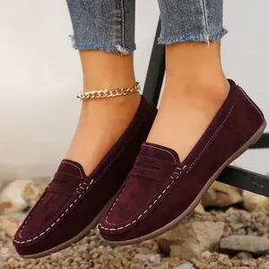 Close-up of stylish burgundy suede loafers with white stitching worn with cuffed blue jeans