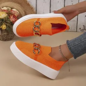 Close-up of orange knit platform slip-on shoes featuring a bold decorative gold chain.