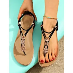 Detailed view of bohemian flat sandals with decorative flowers and black ankle straps
