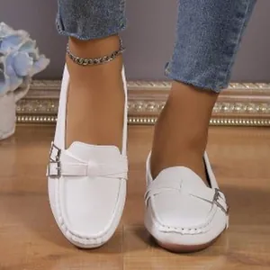 Elegant women's white loafers with buckle detail shown on feet in a lifestyle studio view
