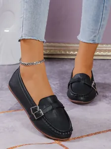 Detailed close-up of black leather loafers with silver buckle and flat rubber sole.