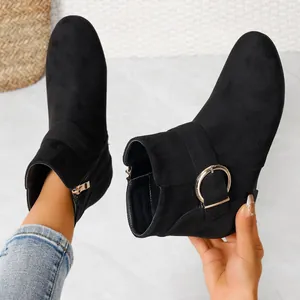 Detail of black Chelsea boots featuring a round gold buckle and side zipper closure.