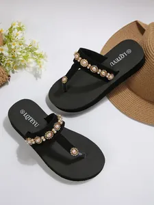 Close-up of black platform flip-flops with pearl flower ornaments and straw hat decor