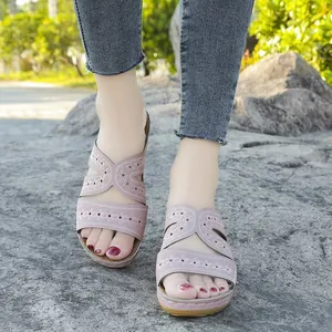 Primer plano detallado de sandalias con cuña bordadas en rosa sobre un suelo rocoso