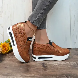 Primo piano di sneakers platform da donna in bronzo con stampa serpente e suola bianca.