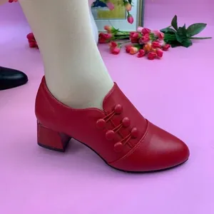 Close-up detail of red chunky heel pump shoe with elegant button accents and smooth finish