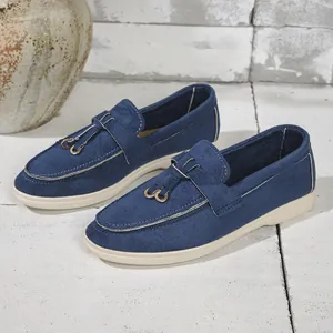 Detail view of blue corduroy loafers with vintage gold buckle on a stone background