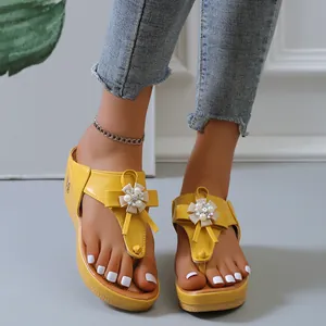 Vista frontal de elegantes chanclas amarillas con cuña y adornos de flores de perlas