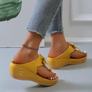 Detalle de chanclas de cuña amarillas para mujer con lazo decorativo y logo B