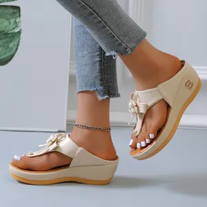 Primer plano de elegantes sandalias beige con cuña, lazo decorativo y perlas