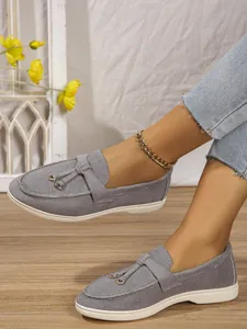 Close-up detail of gray slip-on loafers with tassel accents worn with blue denim jeans