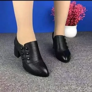 Close-up of black pointed-toe chunky heel boots with crocodile texture and button detail