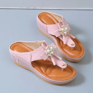 Vista detallada de chanclas rosa con cuña, flor de perlas y logotipo B de metal fino.