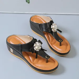Detalle de chanclas de cuña negras para mujer con elegante flor de perlas y lazo