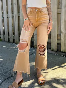 Women's distressed brown jeans with knee rips and raw hem in a casual outdoor setting.