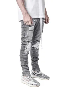 Close-up detail of men's grey distressed skinny jeans with moto style rips and long drawstring