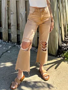 Detail view of women's distressed tan wide-leg jeans with ripped knee design