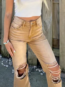 Close-up view of women's tan distressed ripped jeans featuring heavy knee cut-outs and fringe