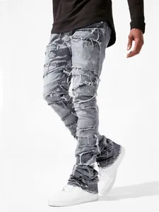 Detail view of men's grey distressed stacked jeans with raw edge patches and slim fit.