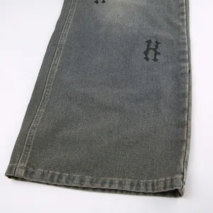 Dettaglio dell'orlo di jeans grigi consumati con la stampa della lettera H gotica