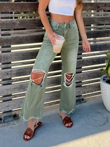 Detailed view of women's sage green distressed wide-leg jeans featuring raw hem.