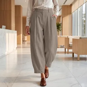 Full-length view of loose pleated khaki harem pants styled with brown loafers in a lobby