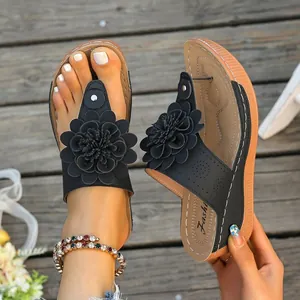 Nahaufnahme von schwarzen Keilsandalen mit einer großen dekorativen Blume auf dem Riemen