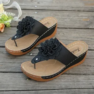 Close-up of elegant black wedge thong sandals featuring a large 3D flower decoration.