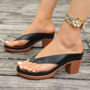 Side view detail of black leather chunky heel thong sandals for women on a wooden deck