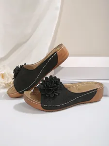 Vue détaillée de sandales compensées noires avec une fleur décorative et talon aspect bois