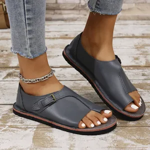 Close-up of grey leather flat sandals with toe loop and metal buckle detail on wooden floor