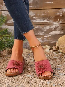 Sandales compensées roses élégantes avec grande fleur sur un fond de gravier naturel.