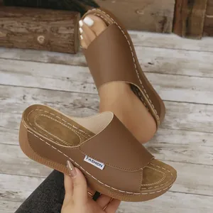 Nahaufnahme einer braunen Keilsandalette mit weißen Nähten und modischem Logo-Etikett