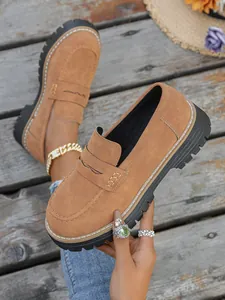 Close-up detail of brown suede loafers featuring thick black soles and white stitching.