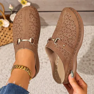Detail view of brown platform mules with floral laser-cut patterns and gold chain accent.