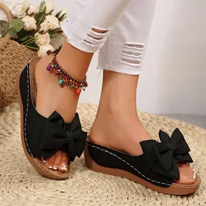 Nahaufnahme schwarzer Sandalen mit Schleife, Keilsohle und weißen Ziernähten.