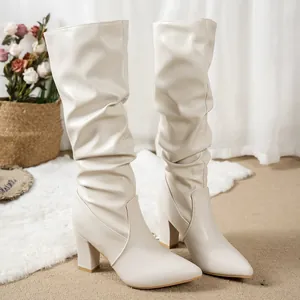Side view of cream pointed toe slouched boots with chunky heels in cozy home setting