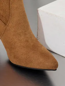 Detailopname van bruine suède-achtige slouchy laars met puntige neus en fijn stiksel.