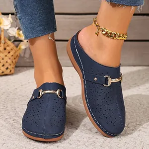 Close-up detail of navy blue mule clogs featuring floral laser-cut patterns and gold buckles.