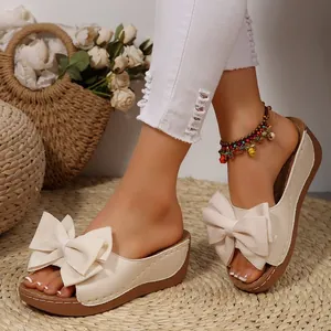 Detailansicht von beigen Keilsandaletten mit Schleife und Boho-Fußkettchen
