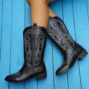 Bottes de cowboy noires élégantes avec broderie blanche sur fond de bois bleu rustique