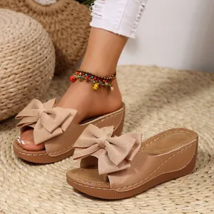 Detailansicht lässiger Damen-Keilsandalen mit Schleife und gewebtem Strohhintergrund.