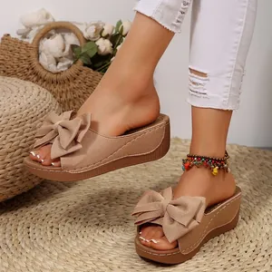 Elegante beige Keilsandaletten mit großer Schleife auf einer geflochtenen Strohmatte.