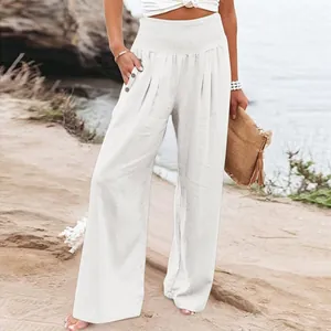 Women's high-waisted white linen wide-leg trousers shown in a stylish beach setting.
