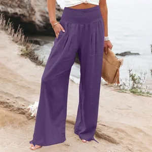 Dettaglio dei pantaloni larghi viola in cotone e lino a vita alta su una spiaggia.