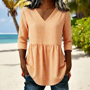 Close-up of orange and white gingham V-neck peplum top on a sunny beach background