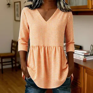 Close-up of a women's orange gingham plaid V-neck blouse with a ruffled peplum hemline