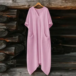 Vista frontal de un vestido largo bohemio rosa suelto colgado en una percha de madera.